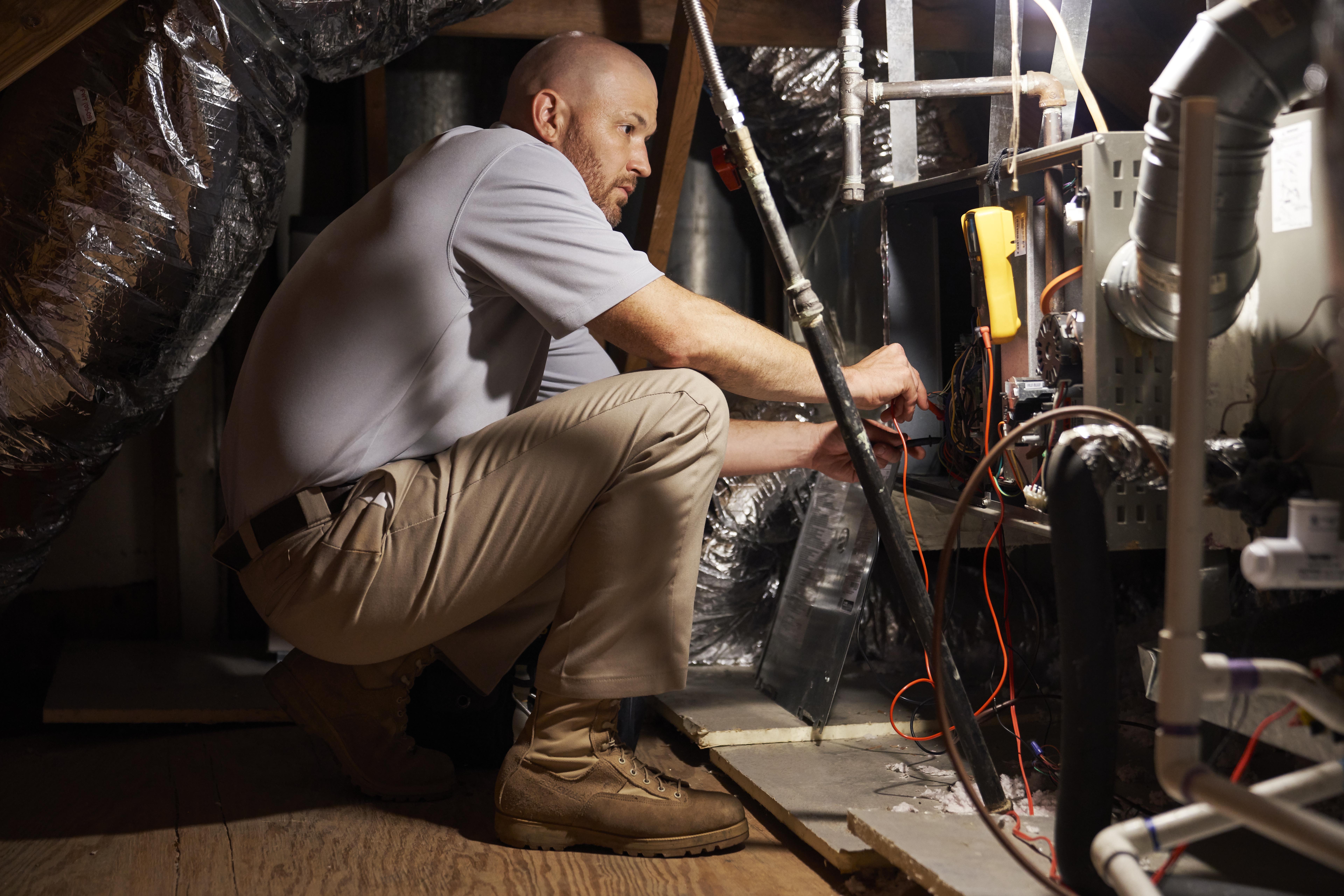 HVAC technician in an attic repairing a heating system