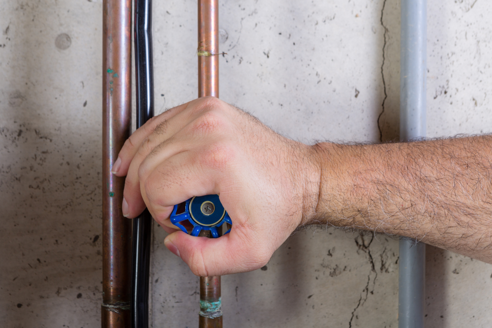 a man's hand turning the water shut-off valve