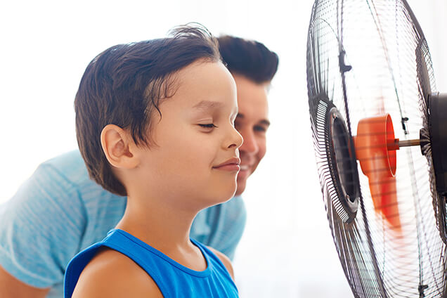 boy sitting in front of the fan