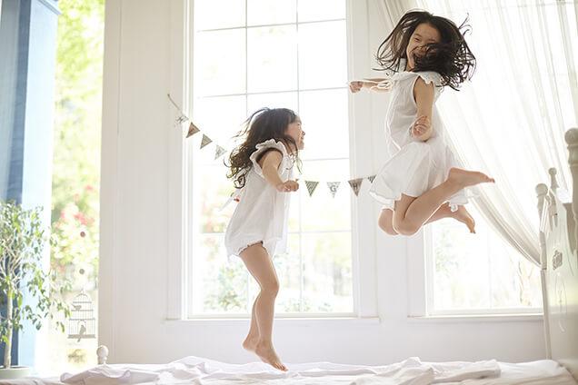 girls jumping on the bed enjoying air conditioning